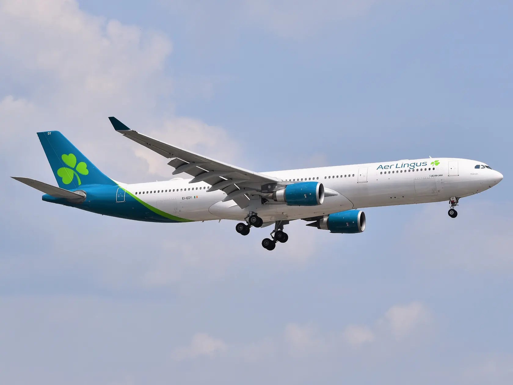 Aer Lingus Airbus A330-302 aircraft EI-EDY with green shamrock logo approaching Newark Liberty International Airport against a cloudy sky.