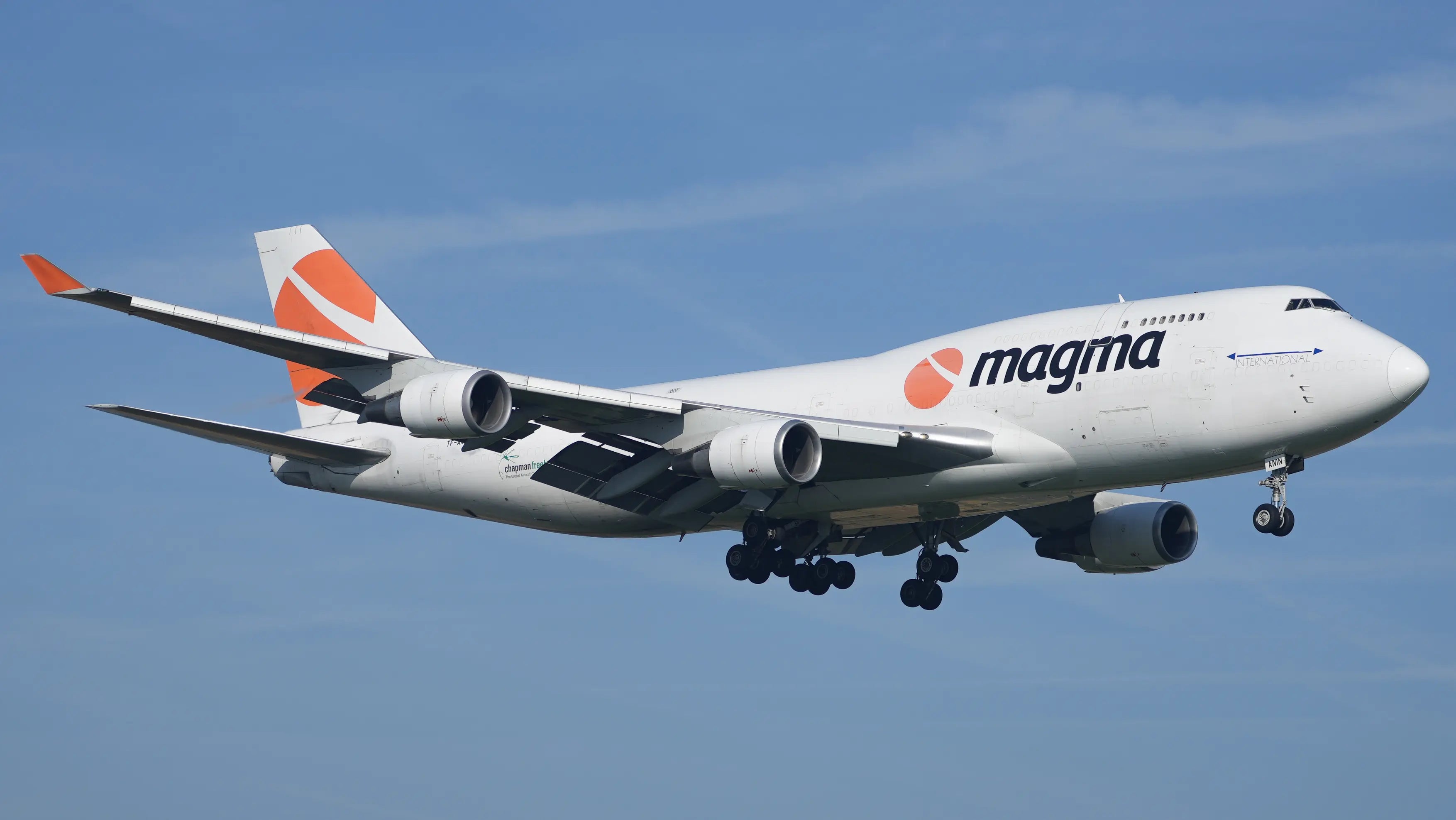 Airborne Boeing 747-4F6 with Magma livery on approach at Liège Airport, featuring four engines and distinctive orange logo on the tail.