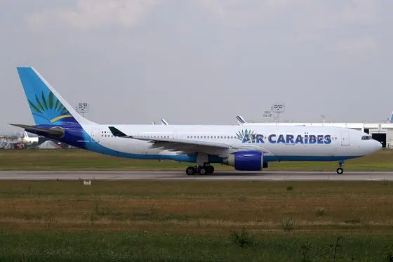 Air Caraïbes Airbus A330 aircraft on the runway with distinctive blue and green tail design, airport terminal and control tower in the background.