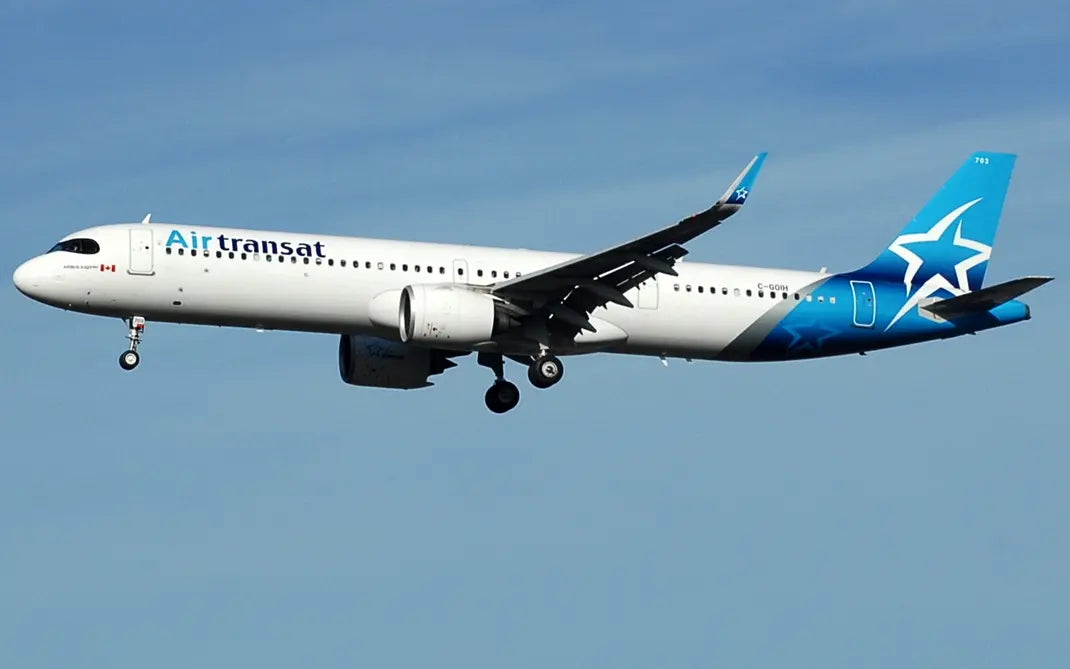 Air Transat Airbus A321 aircraft in flight with landing gear extended against a clear blue sky.