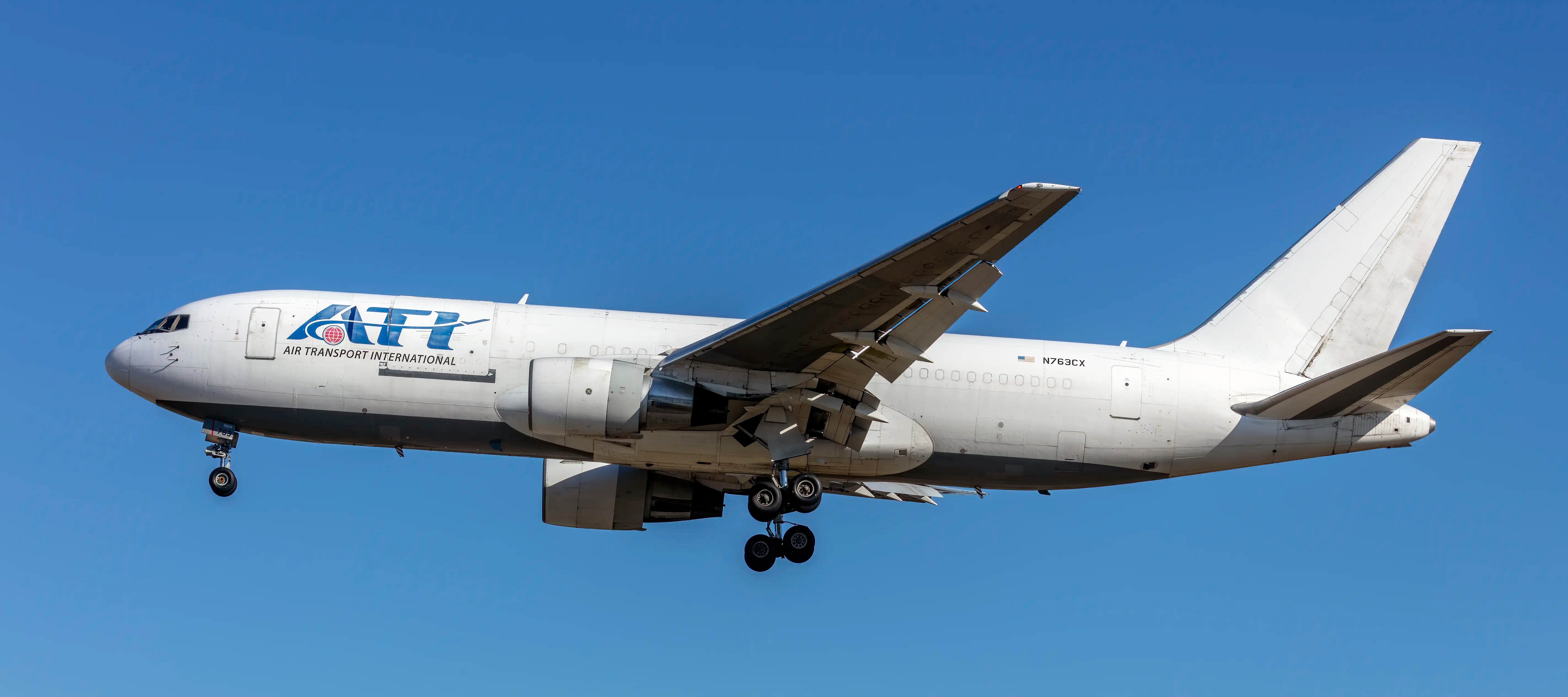 ATI International Boeing 767-200 aircraft in flight, viewed from the side against a clear blue sky with landing gear deployed.