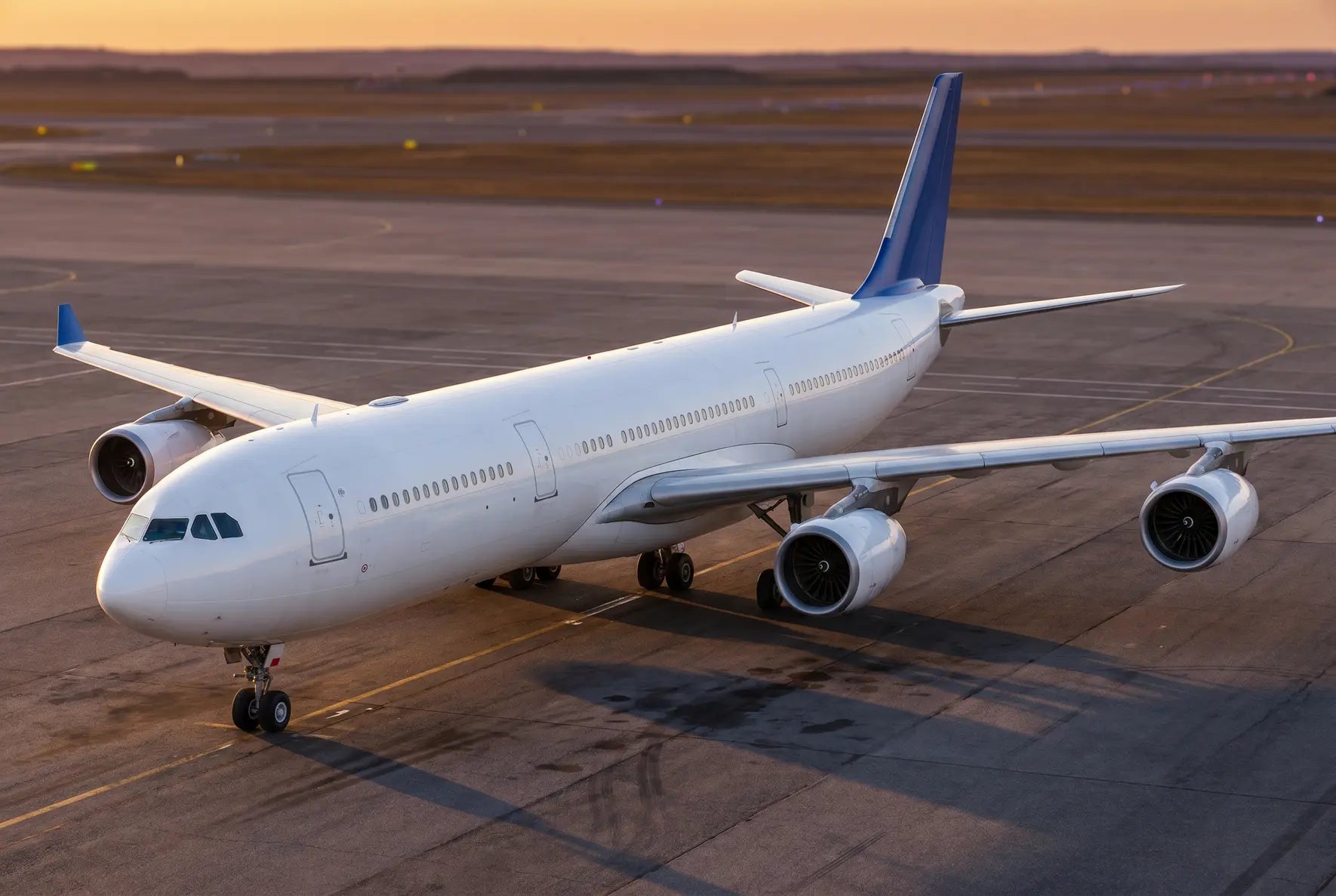 Airbus A340-300 aircraft parked on an airport tarmac during sunset with engines visible and clear sky in background.