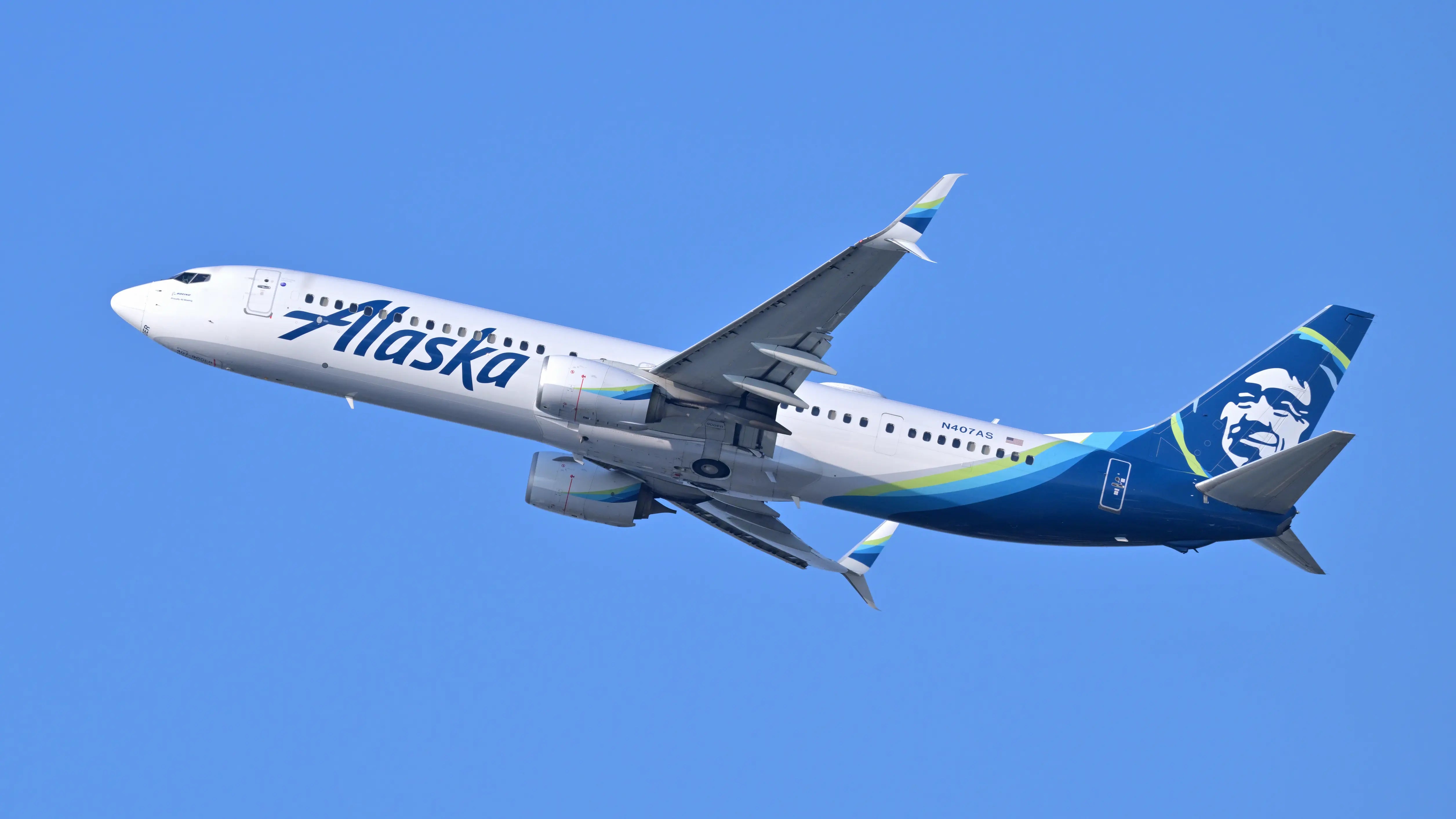 Alaska Airlines Boeing 737-900ER with registration N407AS ascending against a clear blue sky, departing from Boston, June 2025.