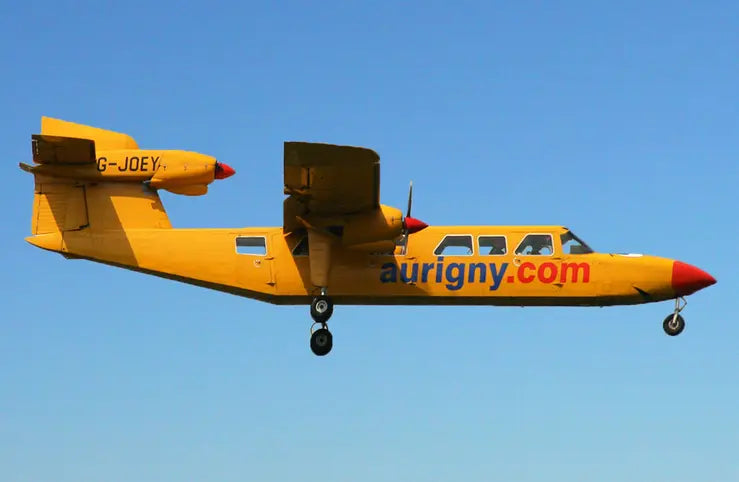 Yellow Aurigny Air Services Britten-Norman BN-2A Mk3 Trislander aircraft in flight, registration G-JOEY, against a clear blue sky.