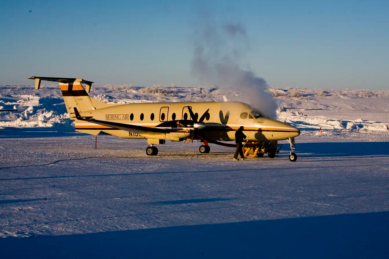 A Beechcraft 1900 aircraft from Bering Air on a snowy runway with ground crew performing maintenance.