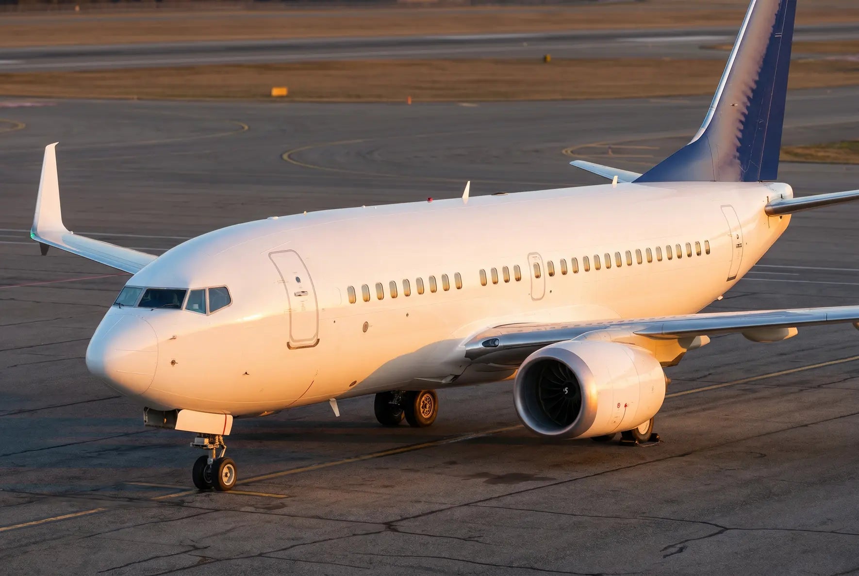 A Boeing 737 MAX 7 aircraft parked on an airport tarmac, illuminated by golden sunset light, showcasing its engines and wings.