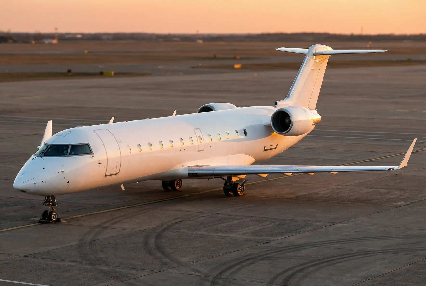 A Bombardier CRJ440 regional jet on the tarmac at sunset, showcasing its sleek design and twin engines with visible landing gear.