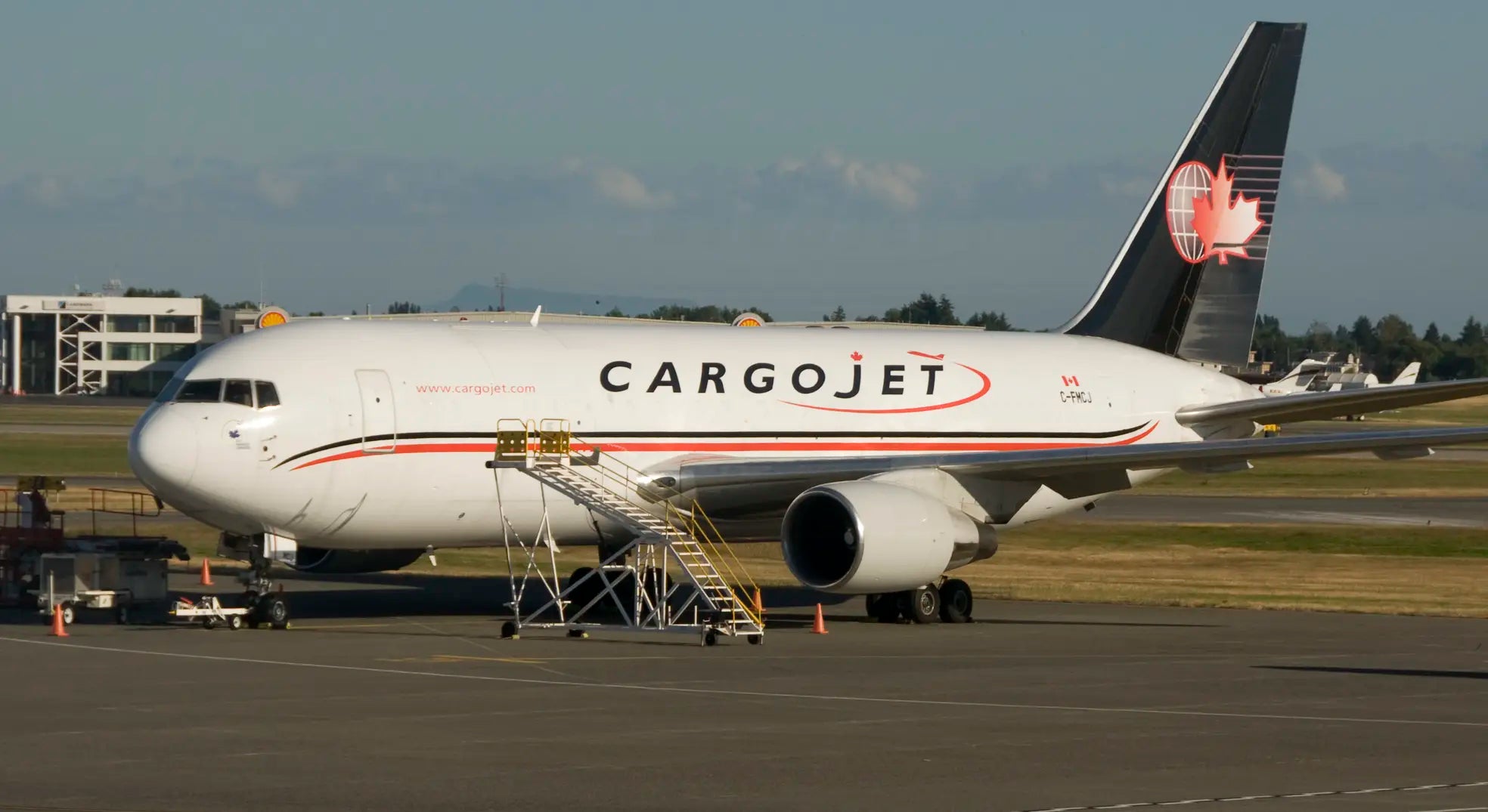 A Cargojet Boeing 767-200 aircraft parked on the tarmac with stairs extending to the door and a clear sky in the background.