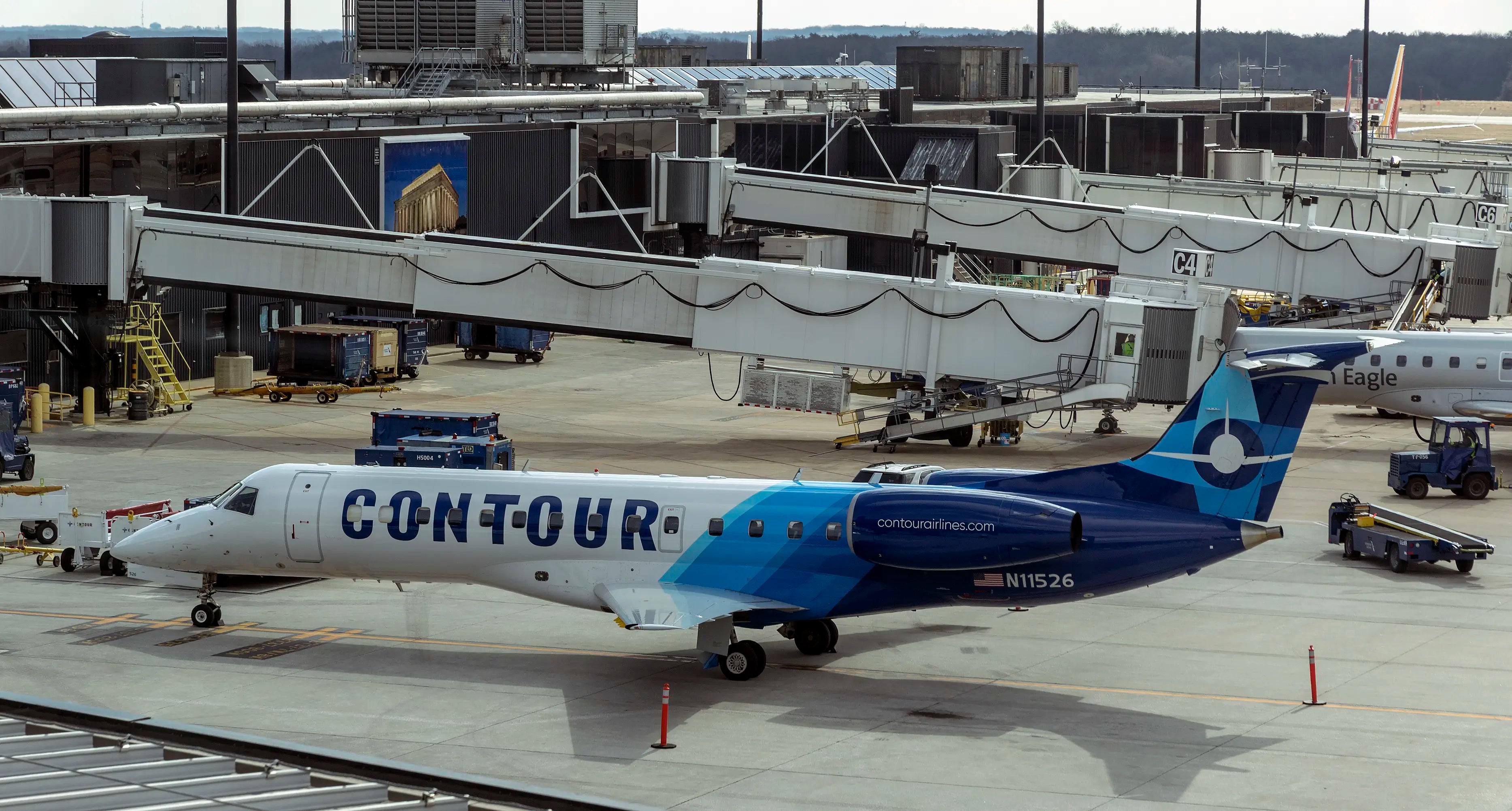 A Contour Airlines plane parked at an airport gate, with jet bridges and terminal buildings in the background.