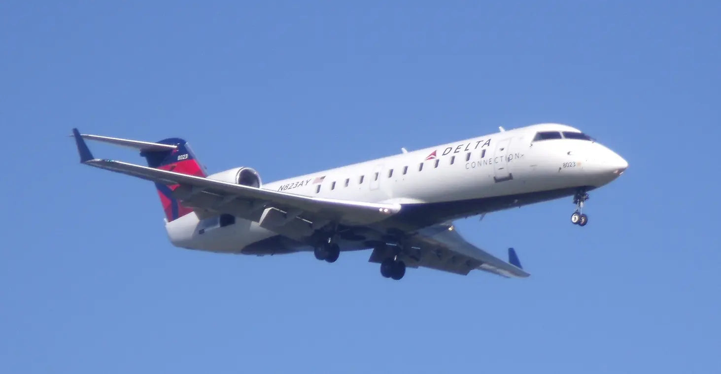 Delta Connection CRJ-200 aircraft in flight, displaying its undercarriage and winglets against a clear blue sky.