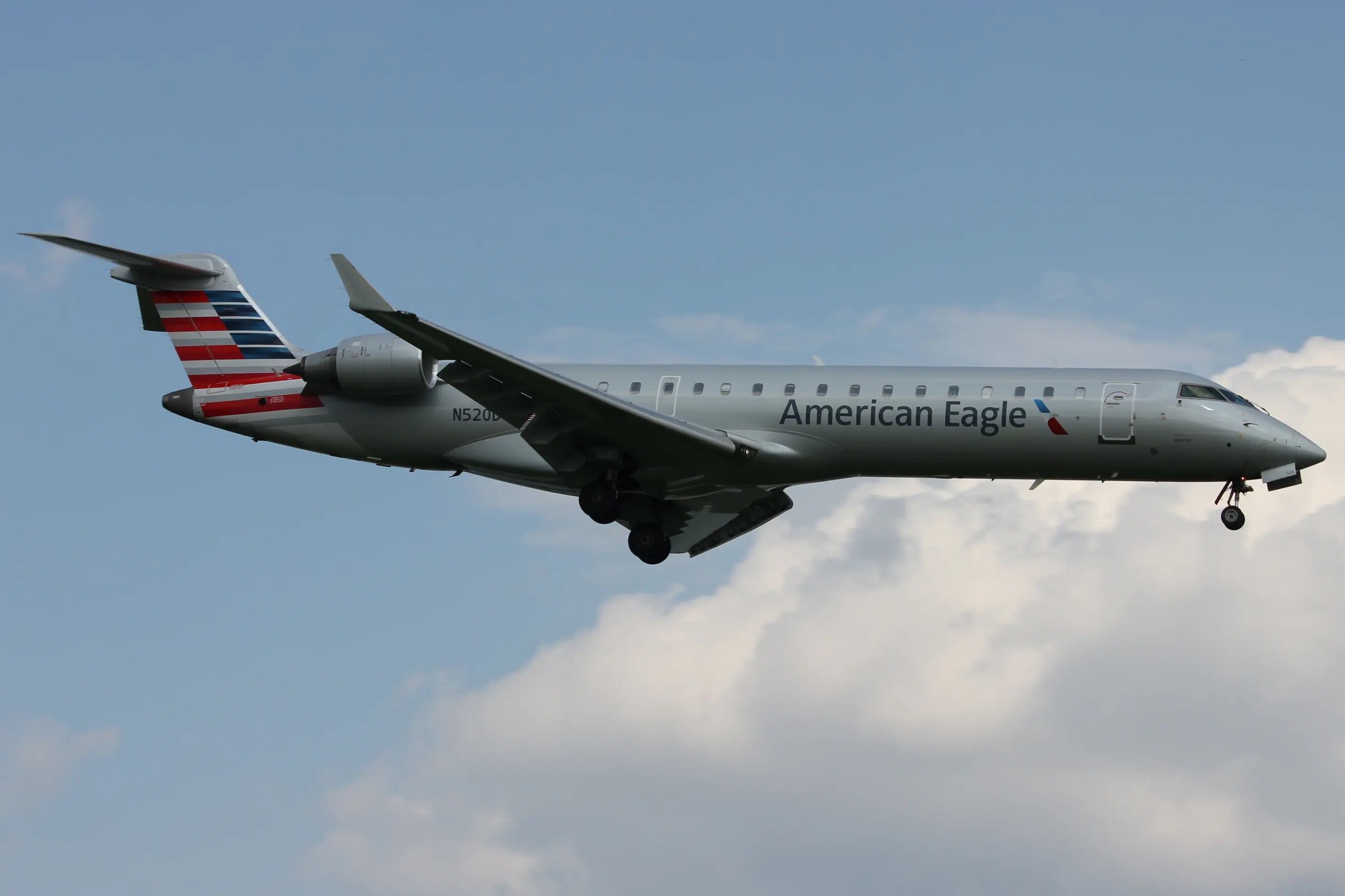 American Eagle airplane in flight with landing gear down against a blue sky with clouds.
