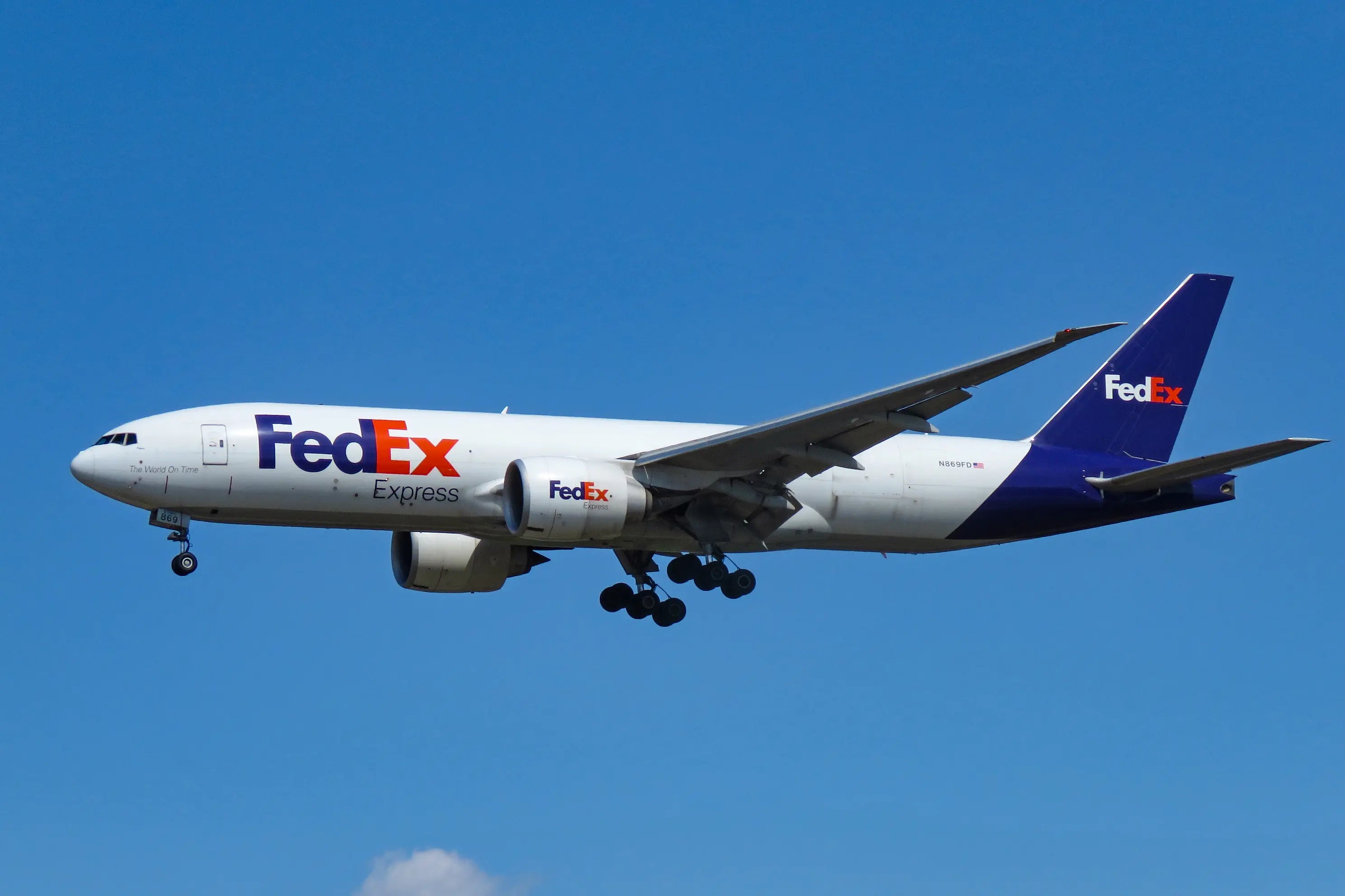 FedEx Express cargo airplane in flight against a clear blue sky, showing the aircraft's side view and landing gear.