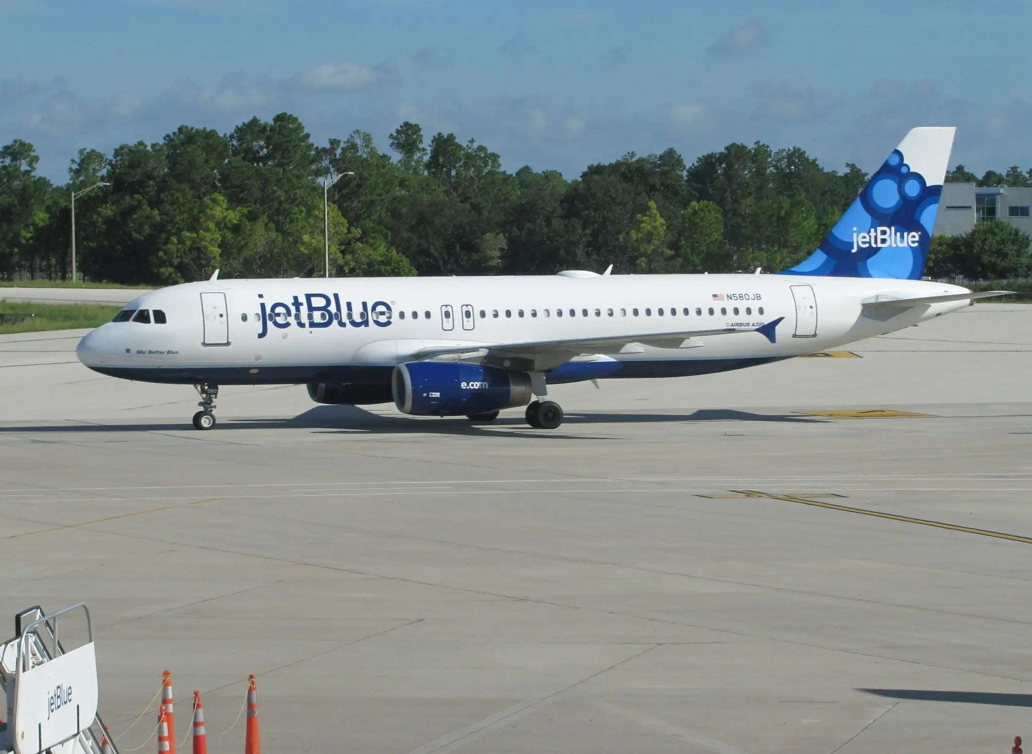 JetBlue Airbus A320 taxiing on the tarmac at Orlando International Airport with trees in the background.