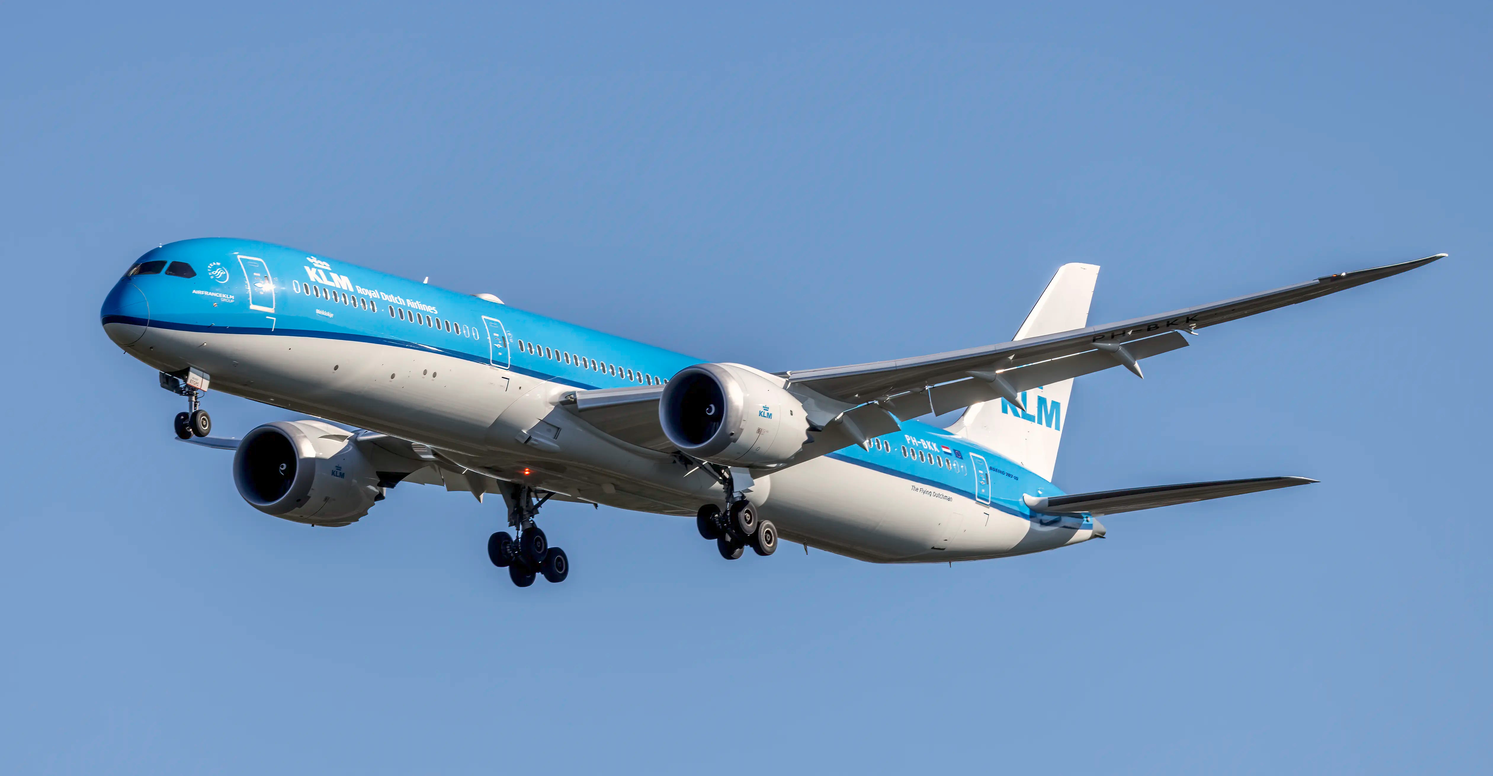 KLM Boeing 787-10 aircraft in flight with a clear blue sky background, showing landing gear extended and engines visible.