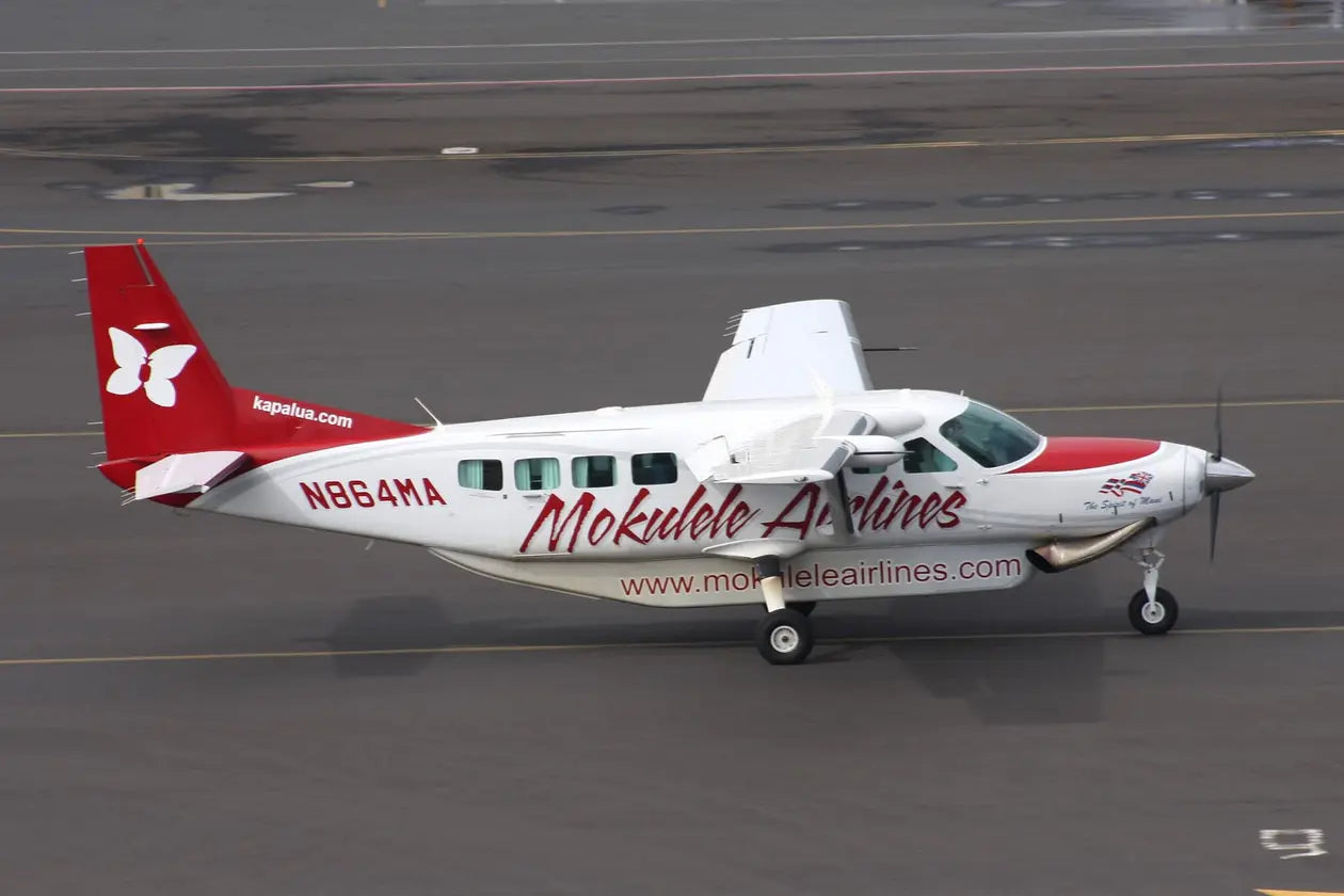 Mokulele Airlines Cessna 208B aircraft, registration N864MA, on the tarmac at Honolulu Airport, featuring red and white livery with butterfly logo.