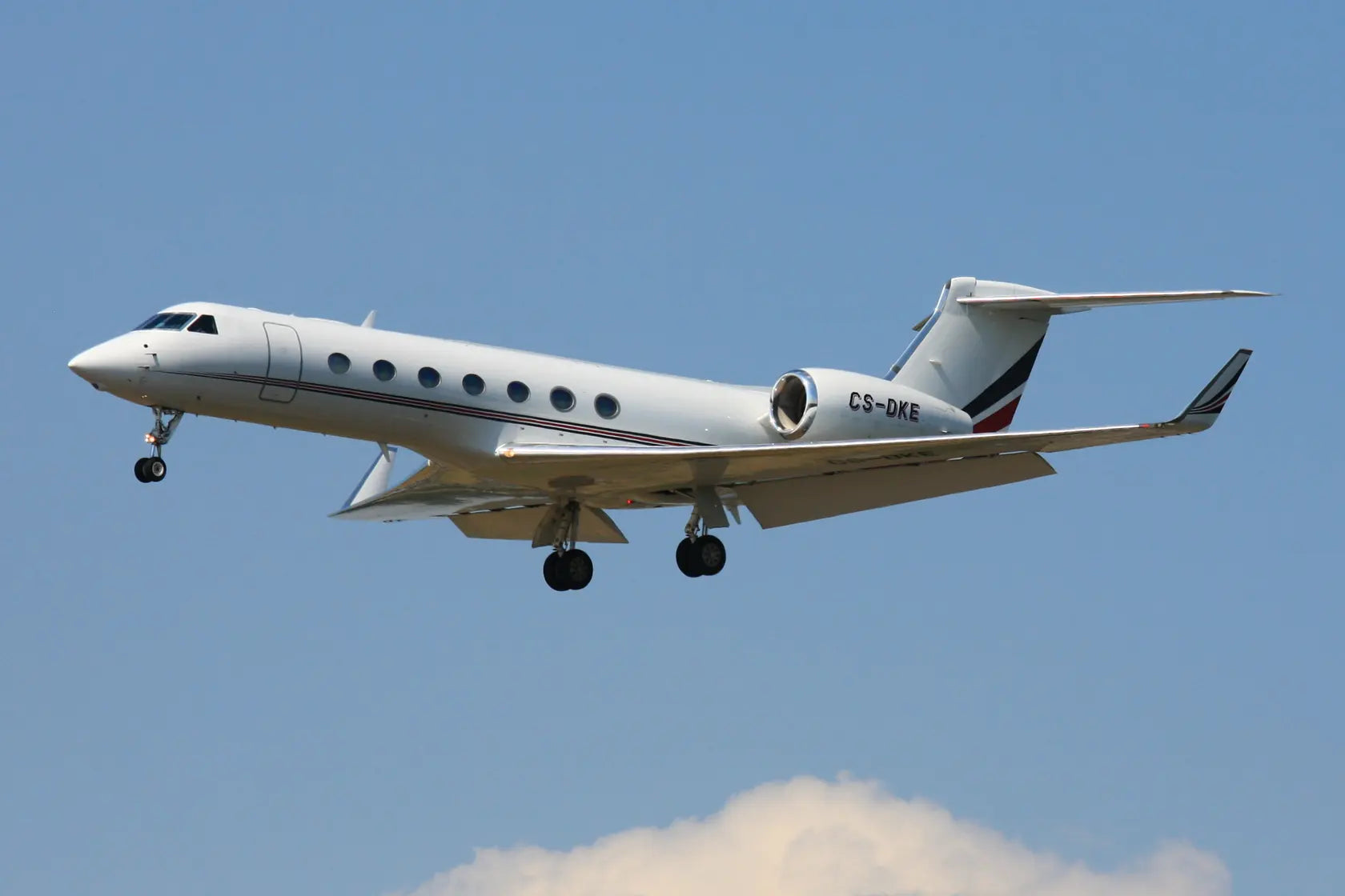 Gulfstream G550 jet in flight with landing gear extended, marked CS-DKE, against a clear blue sky with a hint of clouds.