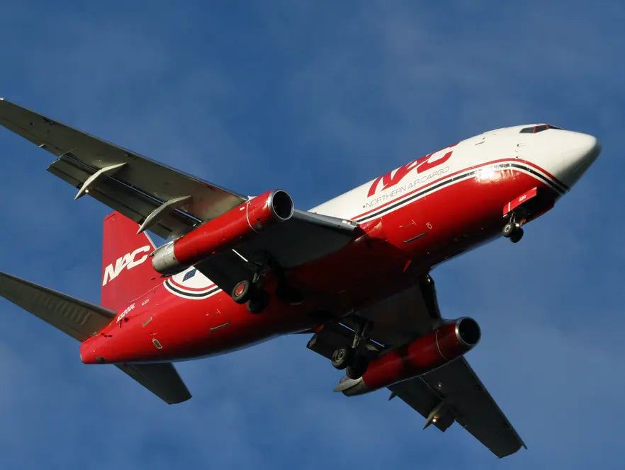 Northern Air Cargo 737 airplane with red and white livery landing at Anchorage Airport against a clear blue sky.