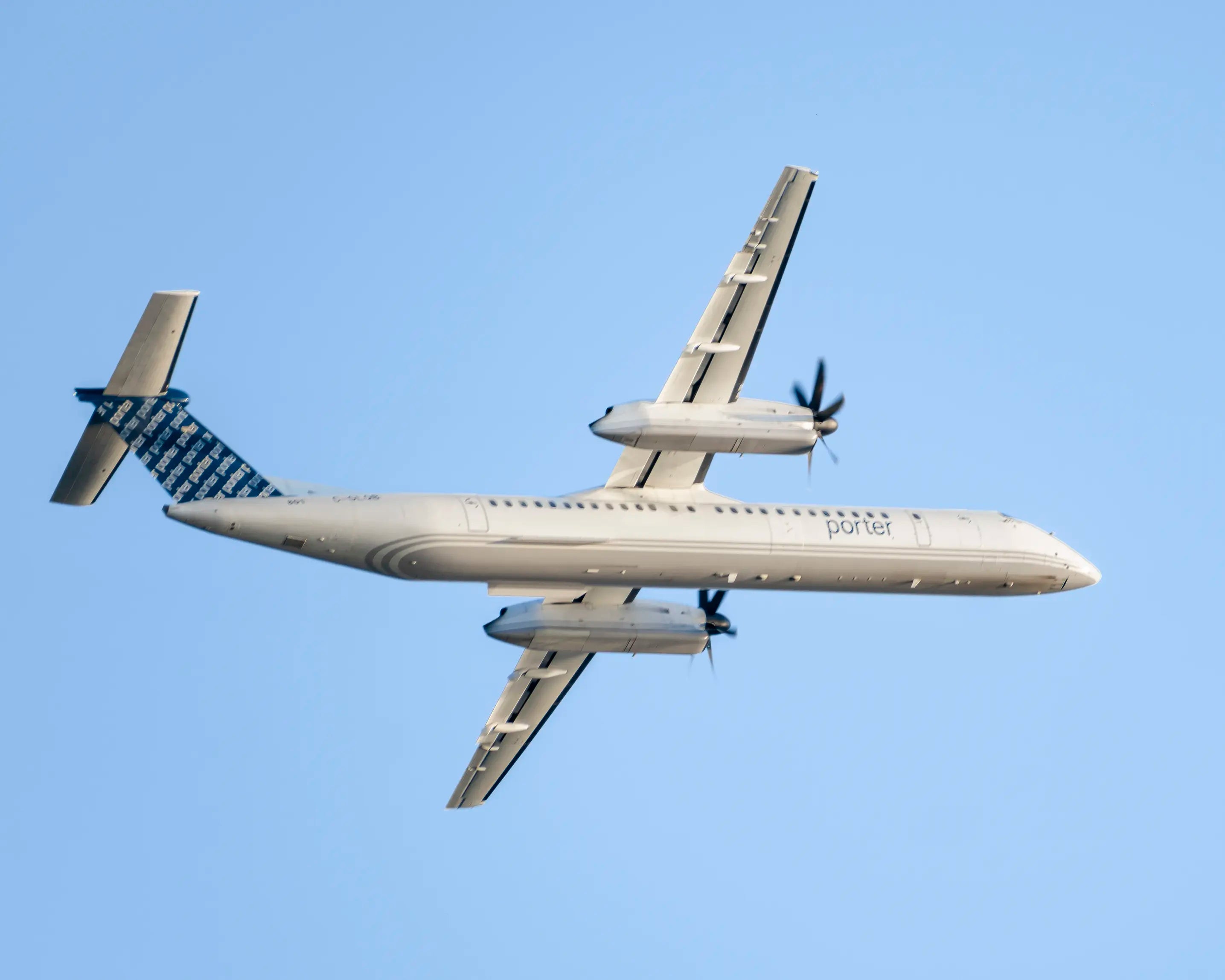 De Havilland Canada DHC-8-400 turboprop airplane of Porter Airlines flying against a clear blue sky.