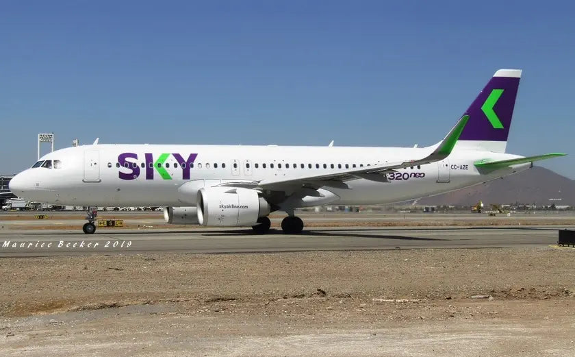 A Sky Airline Airbus A320neo parked on a runway at an airport, showcasing its white fuselage with violet and green branding, under a clear blue sky.