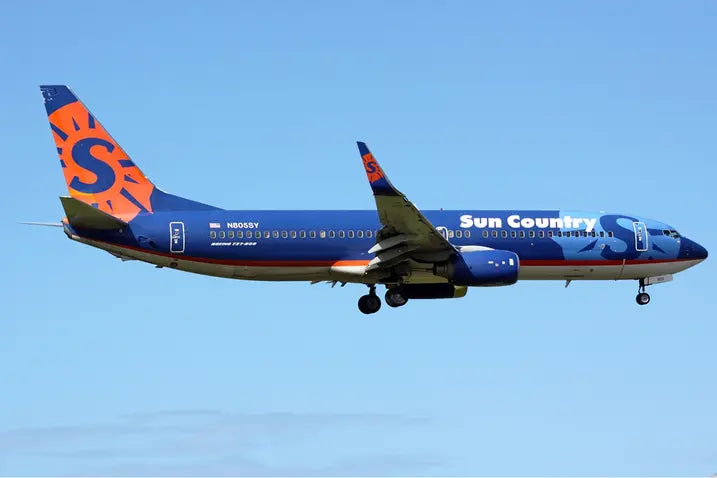 Sun Country Airlines Boeing 737-800 flying against a clear blue sky, featuring a distinctive blue and orange livery with the logo on the tail.