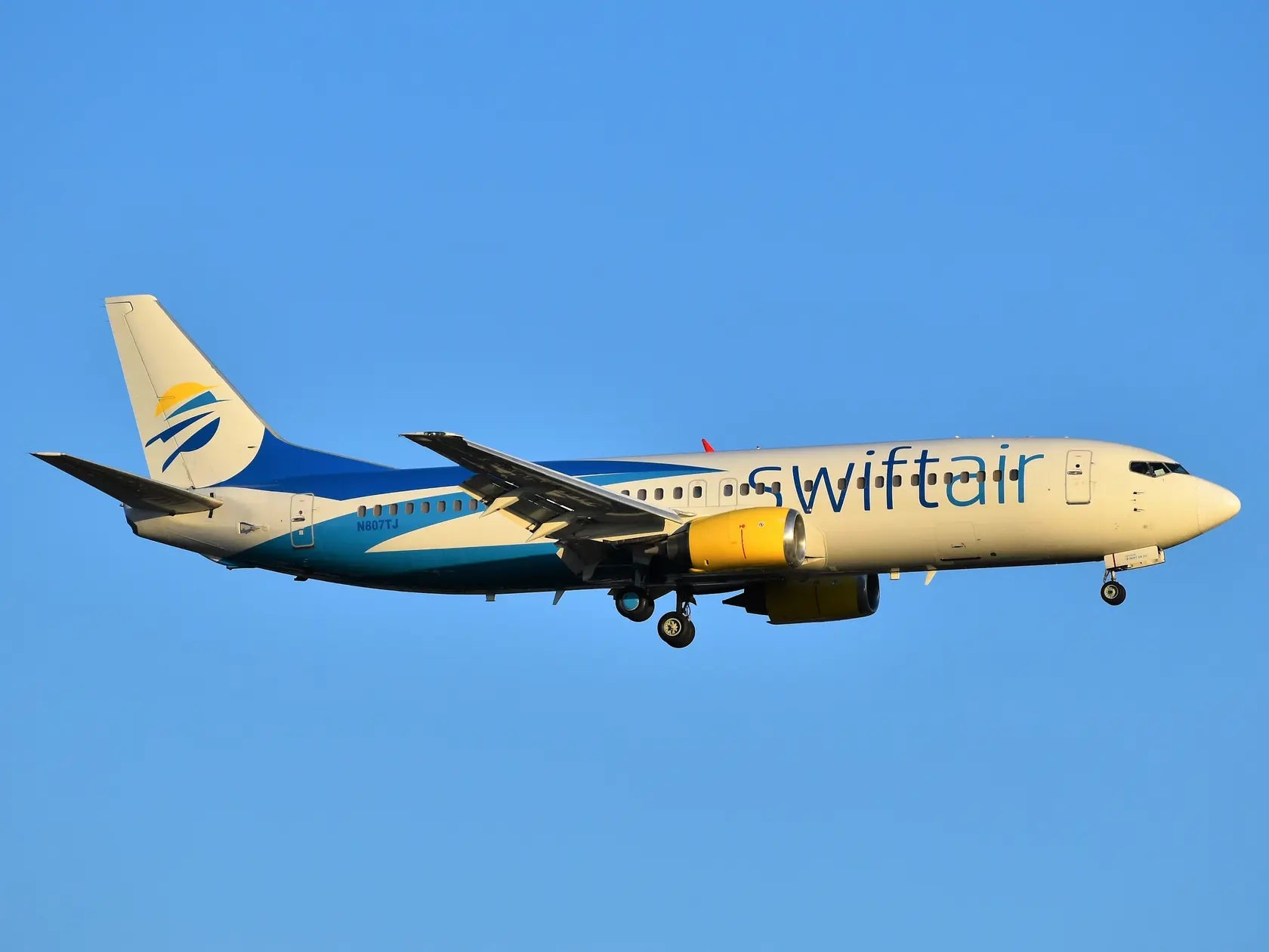 Swift Air Boeing 737-4Q8 aircraft with registration N807TJ approaching JFK Airport against a clear blue sky.