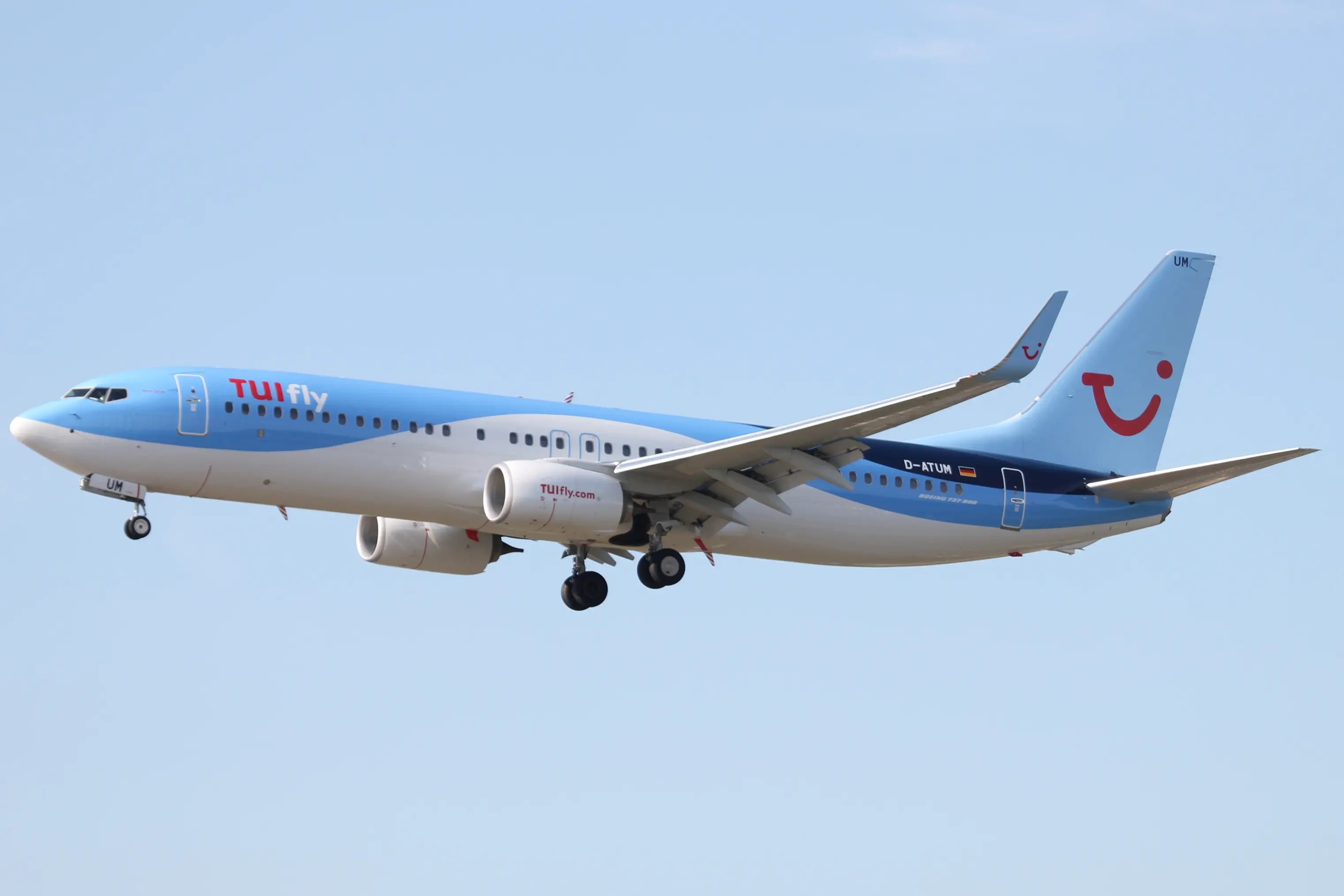 TUI fly Boeing 737-800 aircraft in flight against a clear blue sky, with landing gear extended and distinctive blue and white livery.
