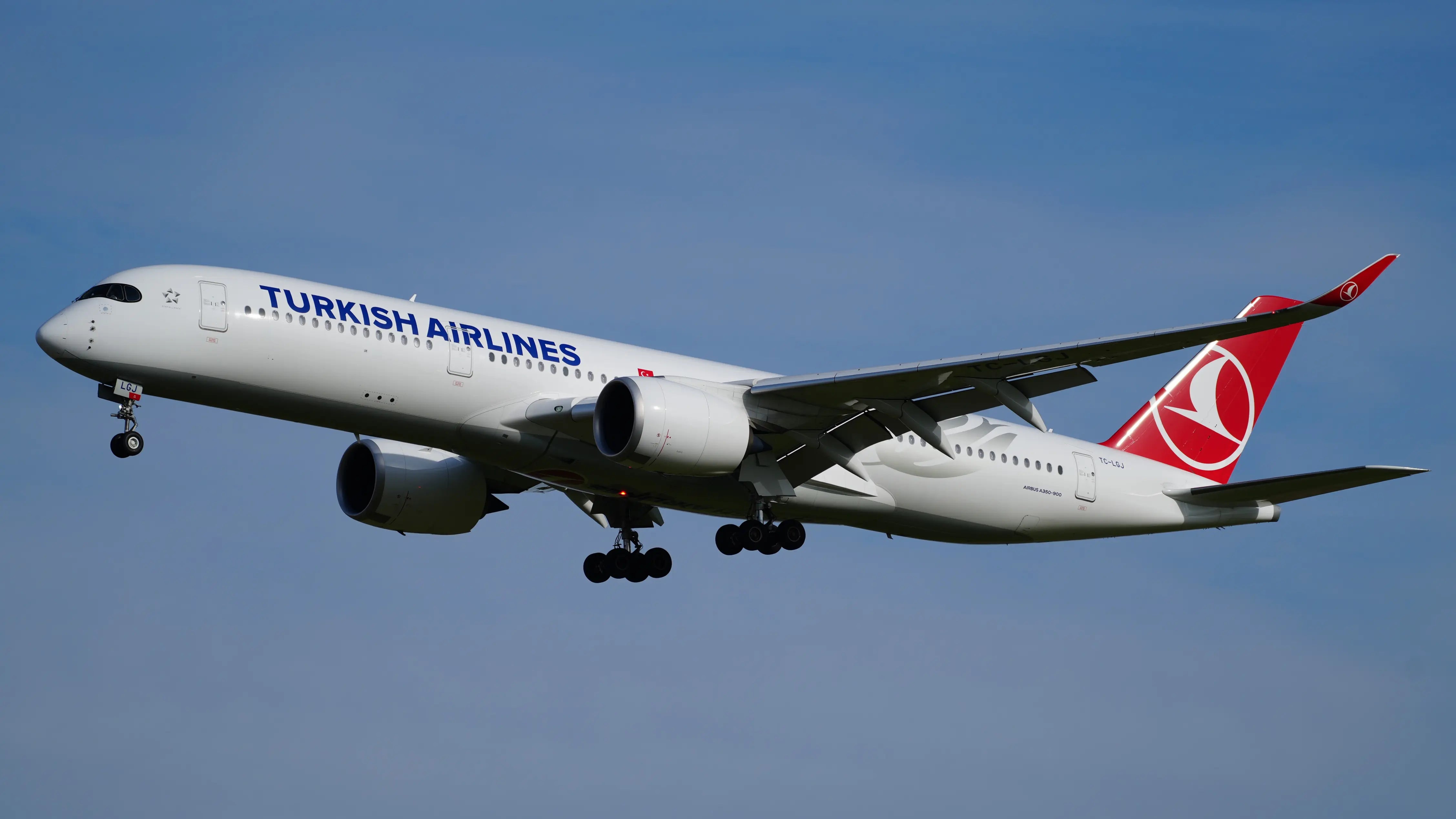 Turkish Airlines Airbus A350-941 in flight against a clear blue sky, showcasing its sleek design and landing gear extended.