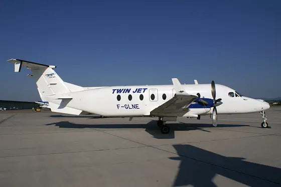 A Twin Jet Beechcraft 1900D airplane labeled F-GLNE is parked on an airport tarmac under a clear blue sky.