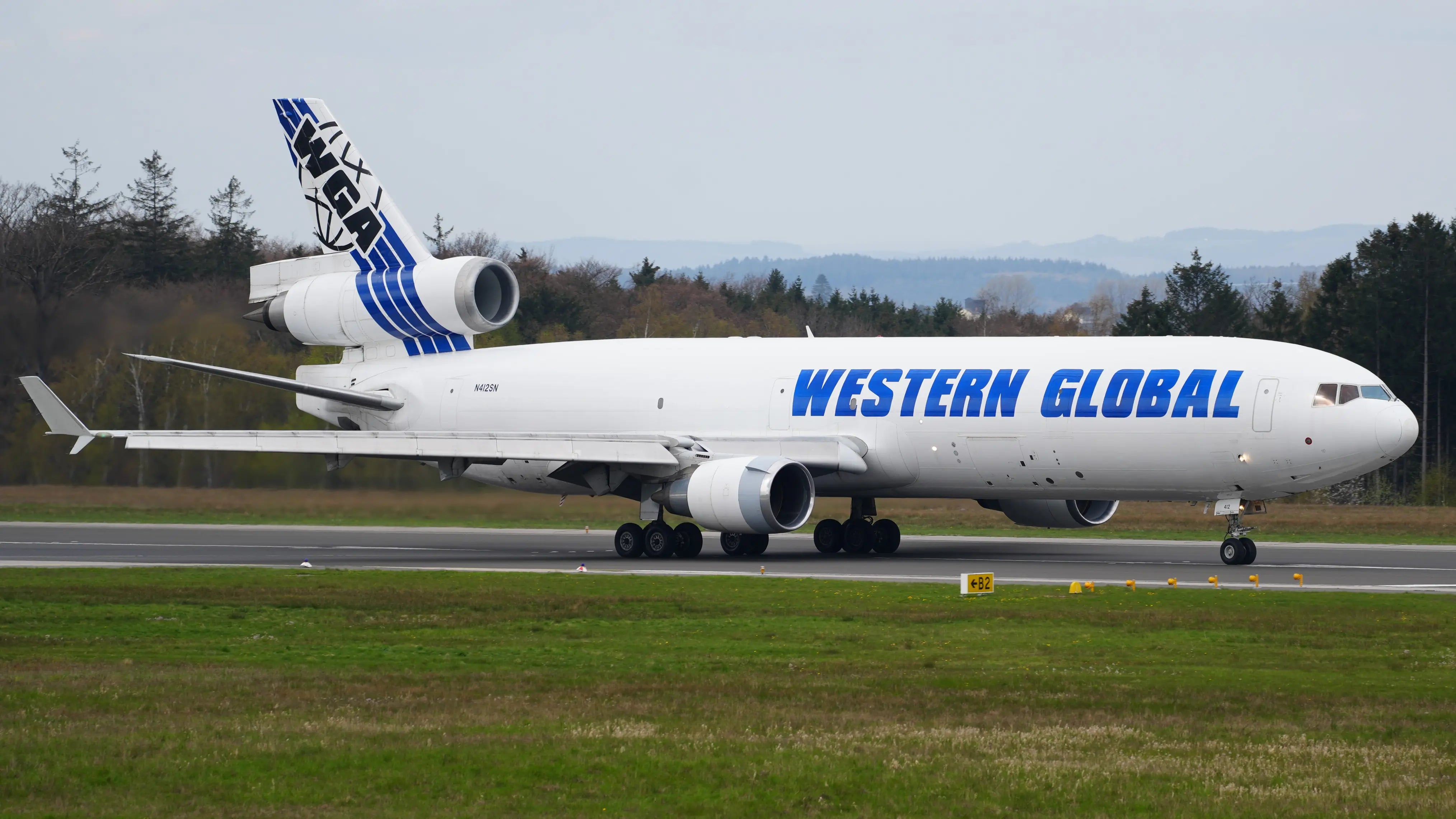 Western Global Airlines McDonnell Douglas MD-11(F) taxiing on runway at Hahn Airport, side view with trees and overcast sky in the background.