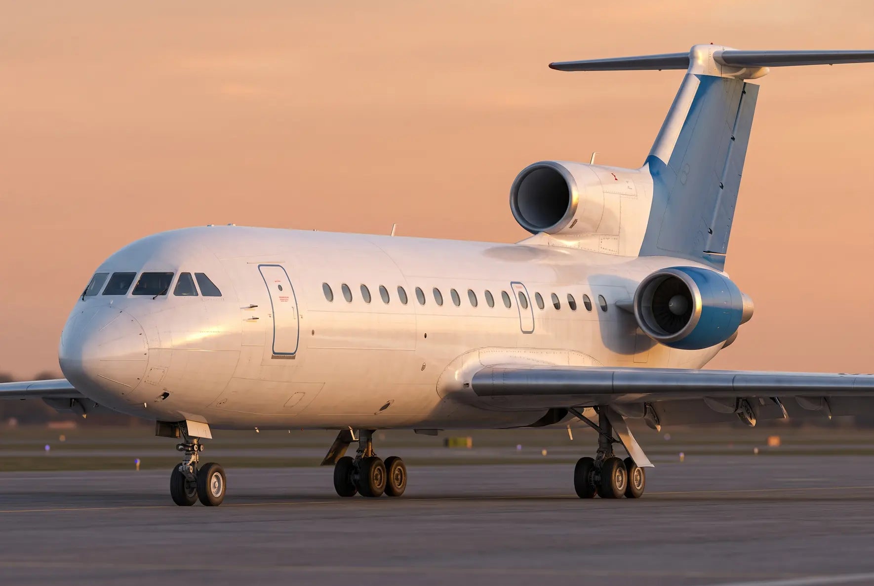 A Yakovlev Yak-42 aircraft on the runway at sunset, showing its three-engine design and distinctive tail with pastel sky in the background.