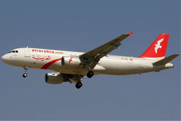 Air Arabia Airbus A320-214 aircraft in flight with visible red and white livery against a clear blue sky.