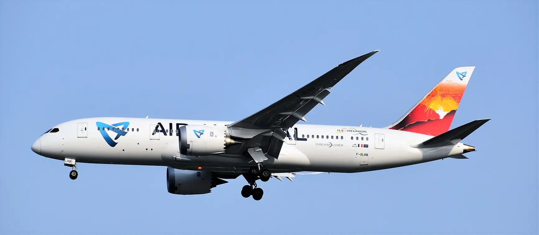Air Austral Boeing 787 Dreamliner in flight, displaying aircraft registration F-OLRB with a detailed tail design against a clear blue sky.