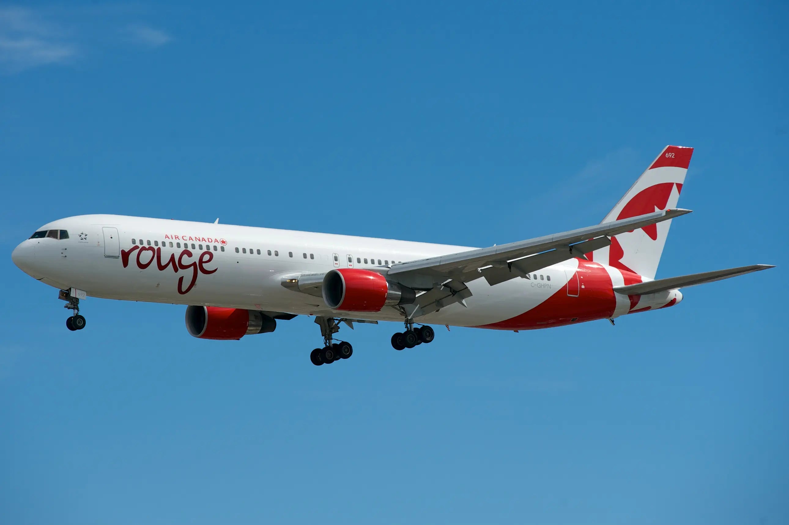 Air Canada Rouge Boeing 767-300ER aircraft in flight with landing gear down against a clear blue sky.