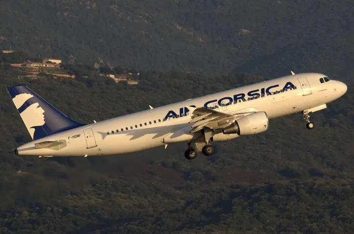 Air Corsica airplane with registration F-HDMF taking off against a backdrop of forested hills.