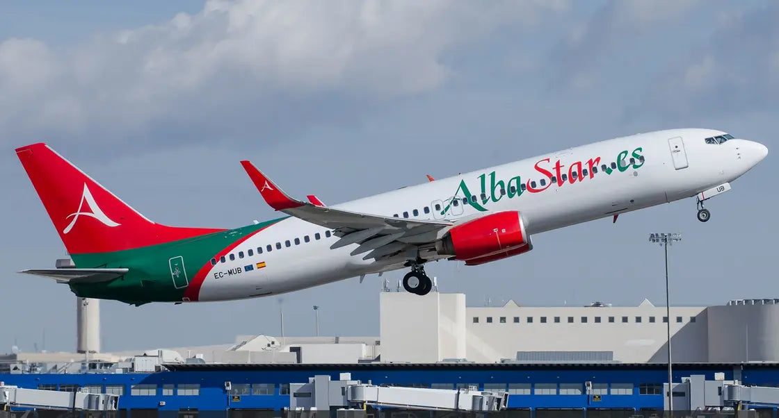AlbaStar-registered Boeing 737 aircraft taking off against a cloudy sky at an airport, showcasing its distinctive red and green livery.