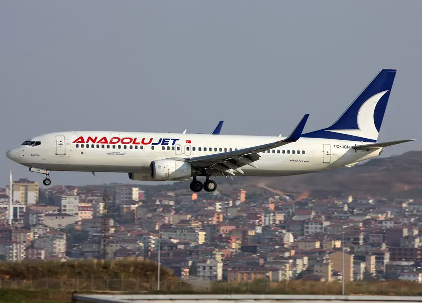 An AnadoluJet Boeing 737-800 aircraft landing at Sabiha Gökçen International Airport with a cityscape in the background.