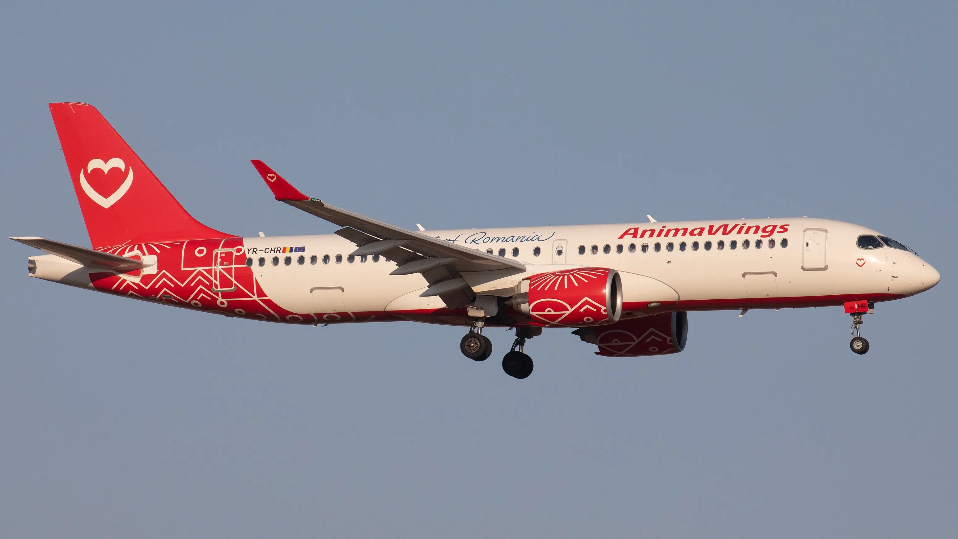 A Animawings Airbus A220 aircraft in flight, featuring the registration YR-CHR and vibrant red and white livery with decorative patterns.