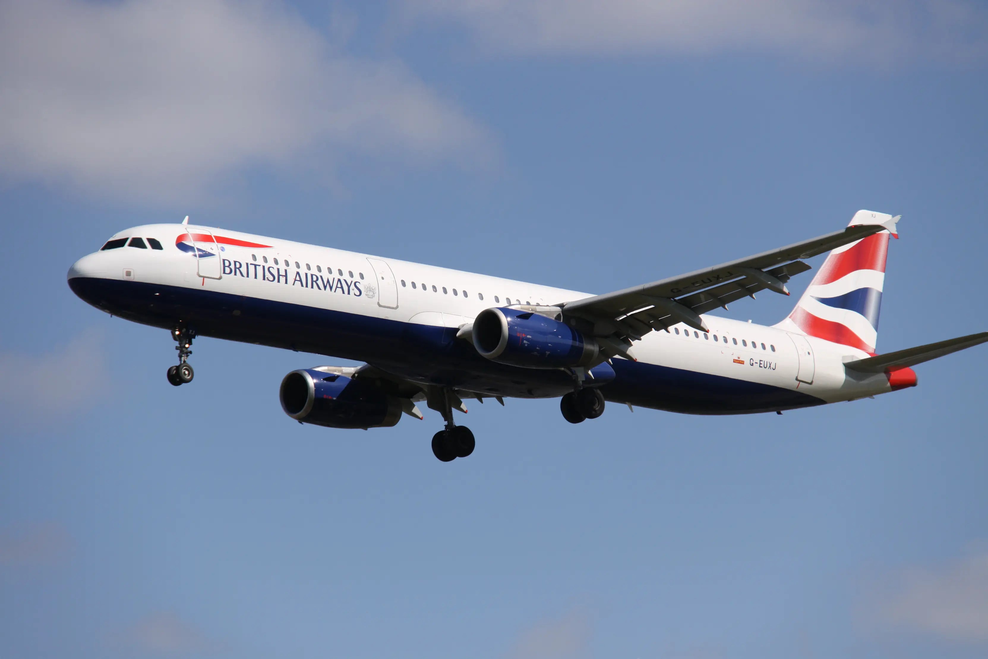 British Airways Airbus A321, registration G-EUXJ, flying in clear blue sky with landing gear extended.