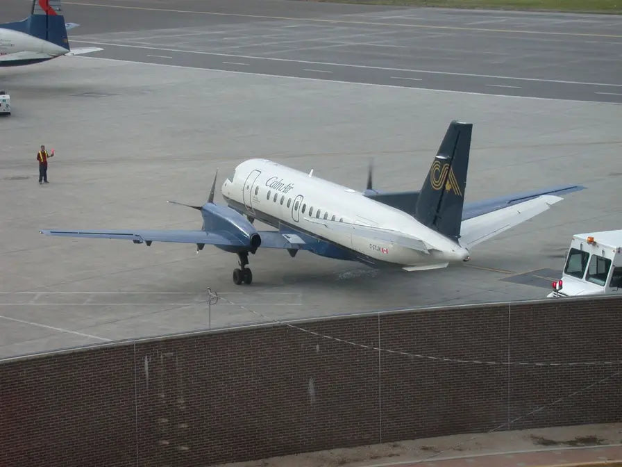A Calm Air Saab 340 aircraft on the tarmac with a ground crew worker directing and a service vehicle nearby.