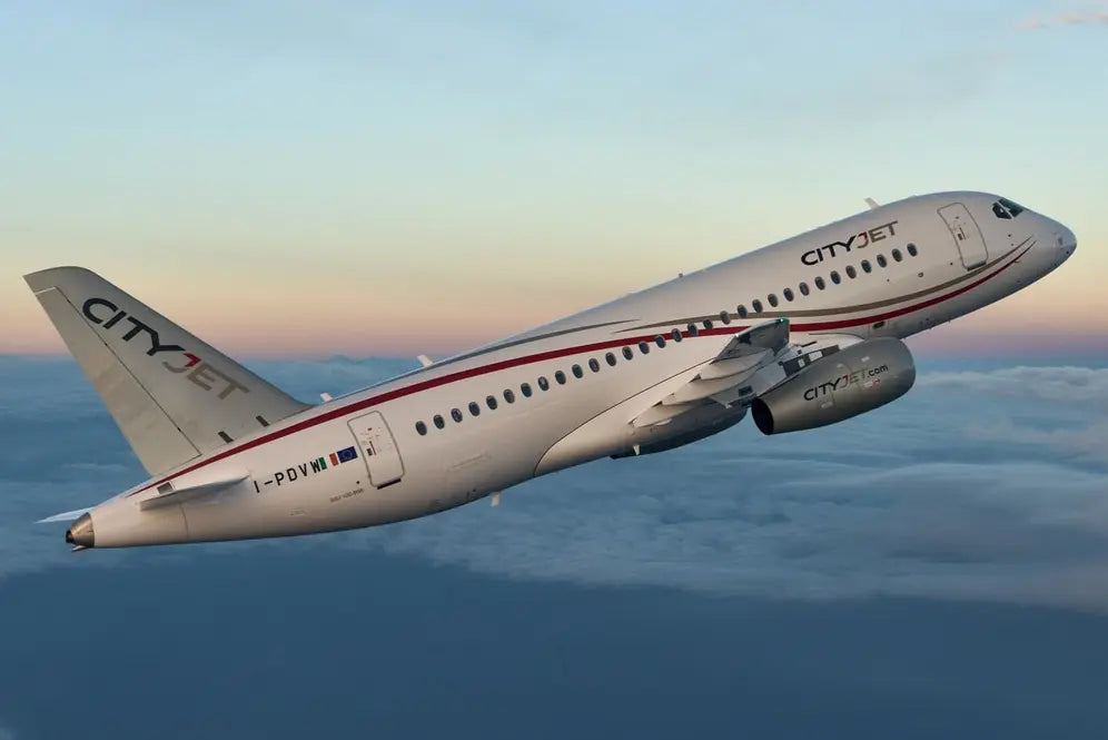 CityJet SSJ100 passenger aircraft soaring above clouds against a colorful sunset sky.