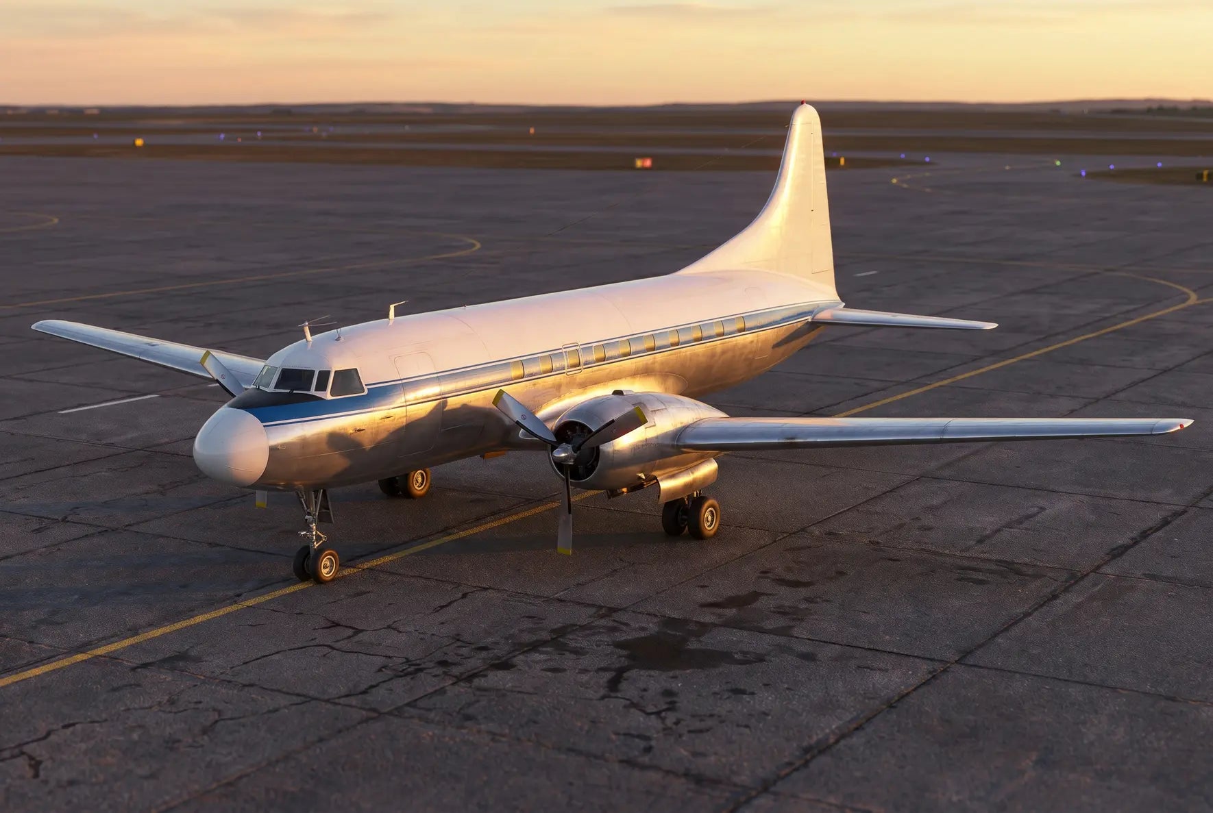 A Convair CV-340 aircraft parked on an airport tarmac during sunset, showcasing its silver body, twin propellers, and streamlined design.