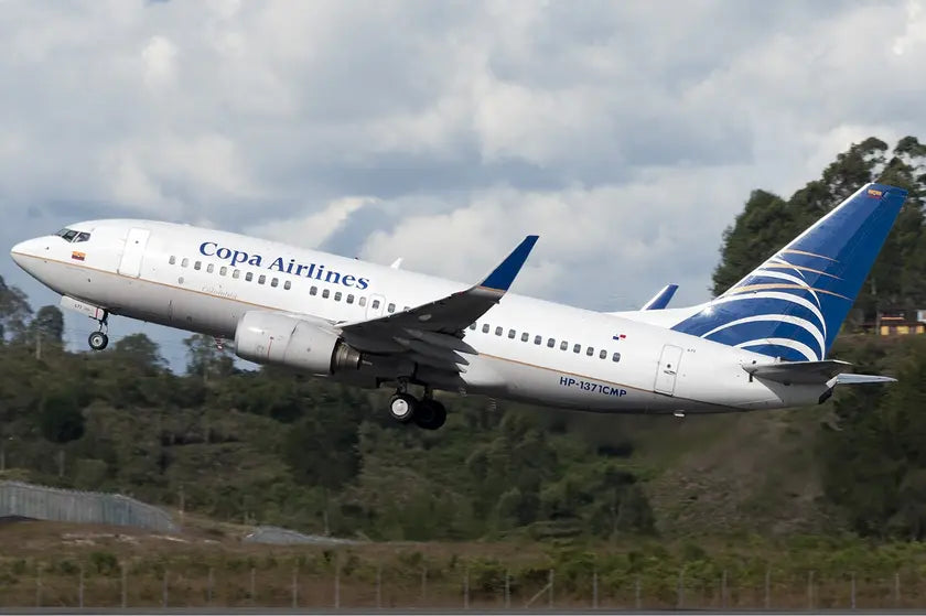 Copa Airlines Colombia Boeing 737-700 taking off from a runway, with landing gear extended and trees in the background under a cloudy sky.