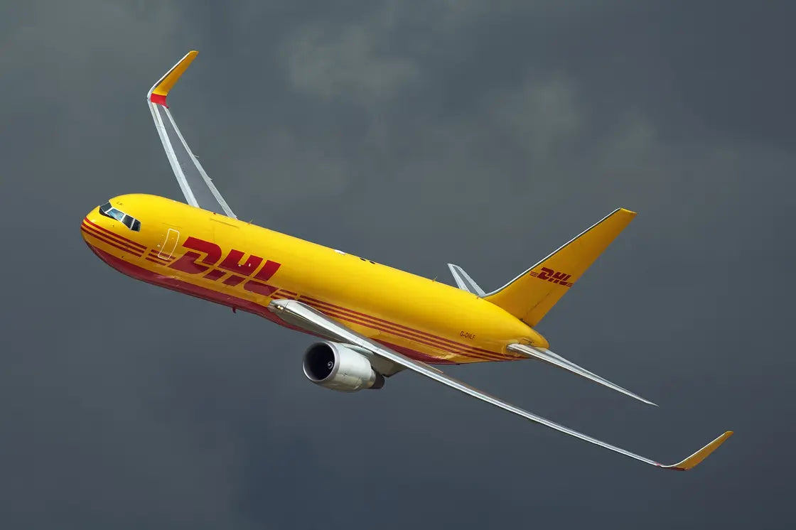 DHL Boeing 767-3JHF cargo plane in flight against a cloudy sky.