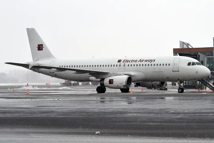 Electra Airways Airbus A320-231 parked on a wet tarmac at an airport, with visible ground handling equipment in overcast weather.