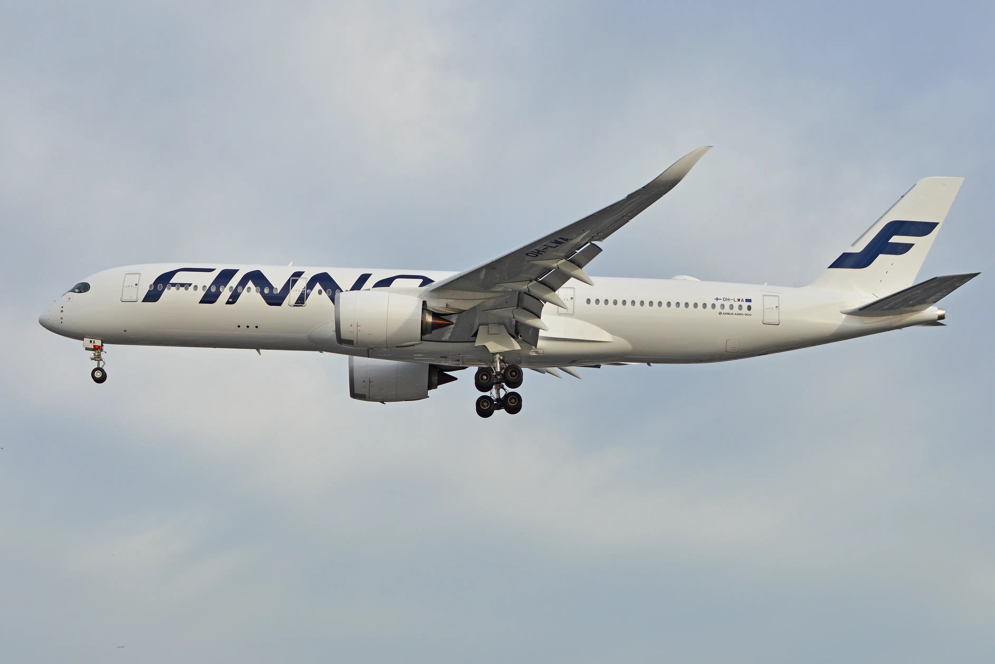Side view of a Finnair Airbus A350-941 aircraft in flight, showing landing gear extended and engines visible, with a cloudy sky background.