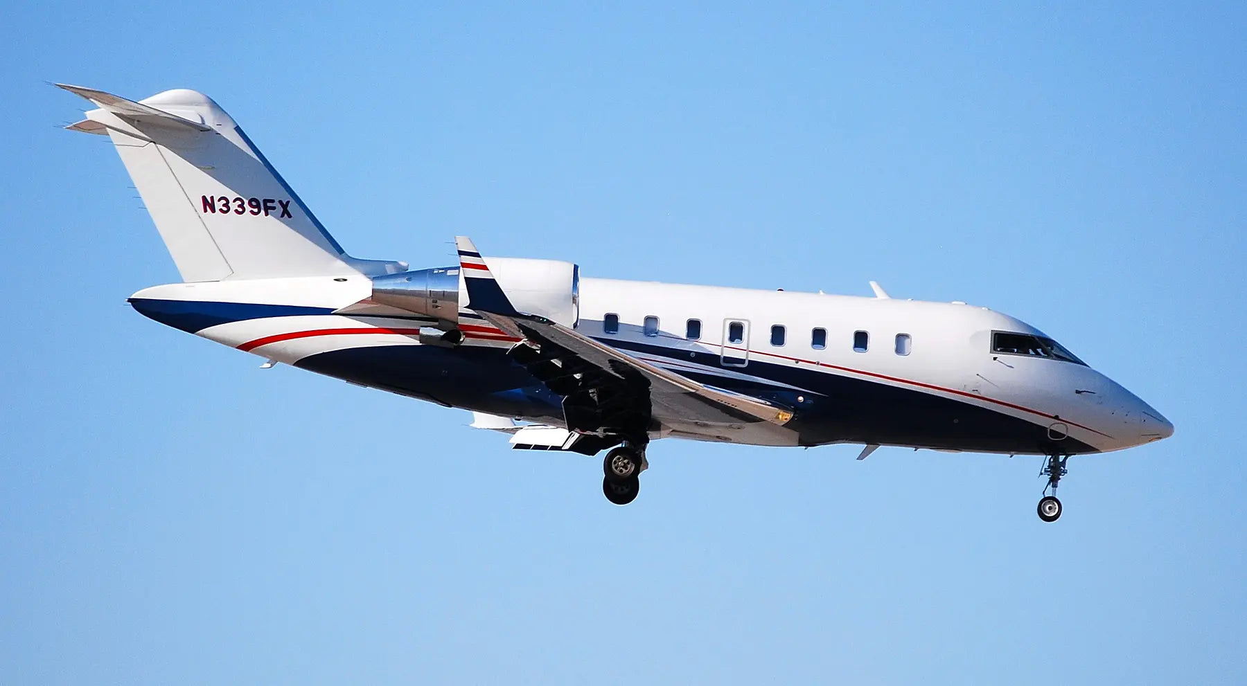 A white and blue Flexjet Challenger aircraft with registration N339FX approaches for landing against a clear blue sky.