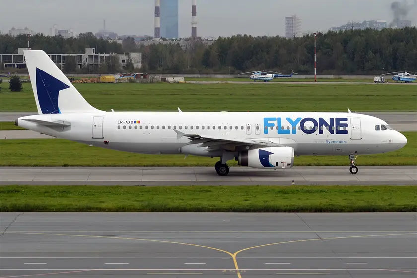 FlyOne Airbus A320-231 airplane ER-AXO taxiing on an airport runway, with green grass in the background and industrial towers visible in the distance.