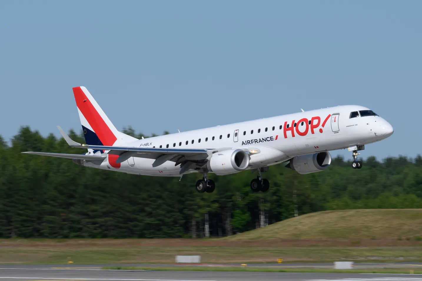 Air France Hop Embraer 190 aircraft F-HBLK landing on a runway with a forest backdrop.