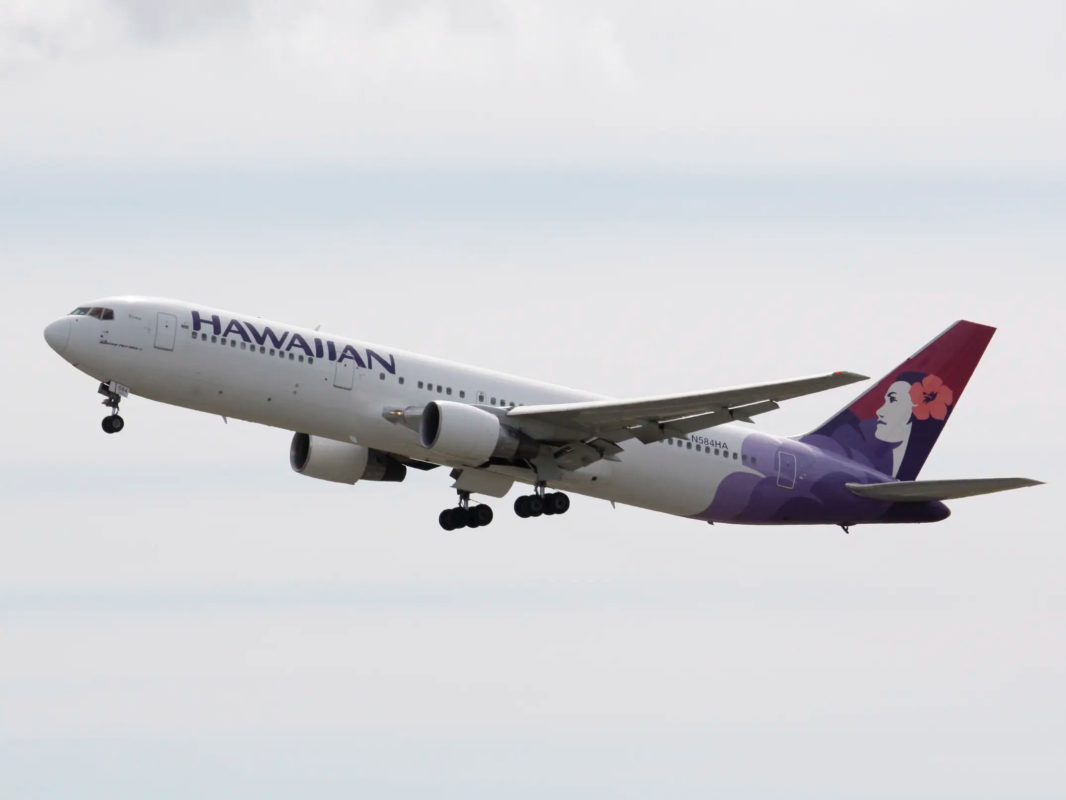 Hawaiian Airlines Boeing 767-300ER in flight, featuring distinctive livery with a woman's head adorned with a red hibiscus on the tail.