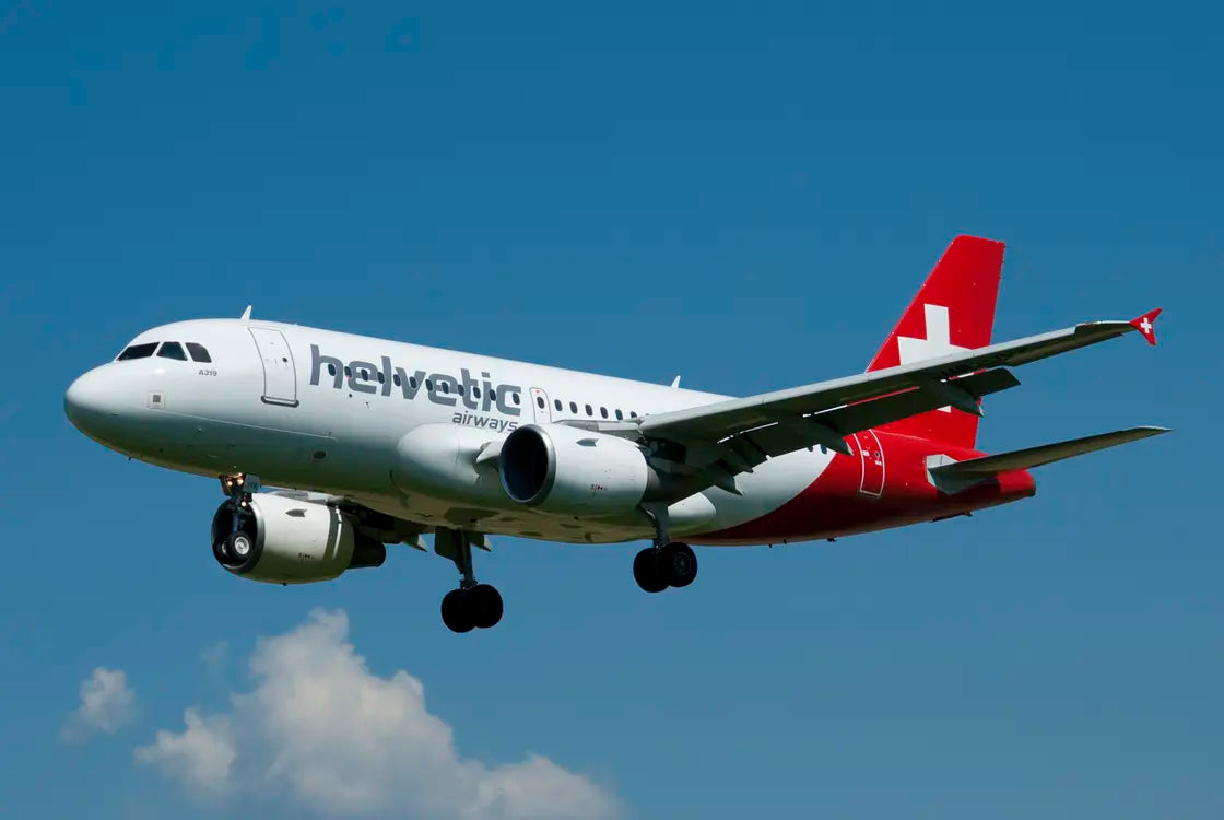 Helvetic Airways Airbus A319 approaching runway 32 at Bern Airport, clear blue sky background, landing gear deployed.